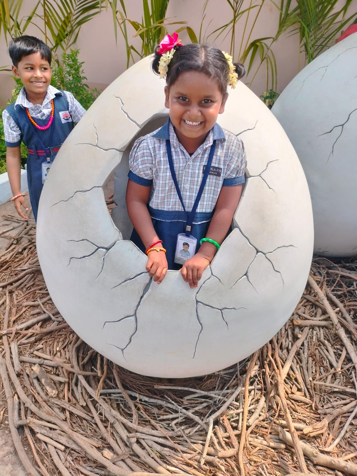 A smiling student peeking out of an egg sculpture on campus